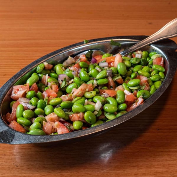 Edamame salad with diced tomatoes and red onions in a silver serving dish on a wooden table.
