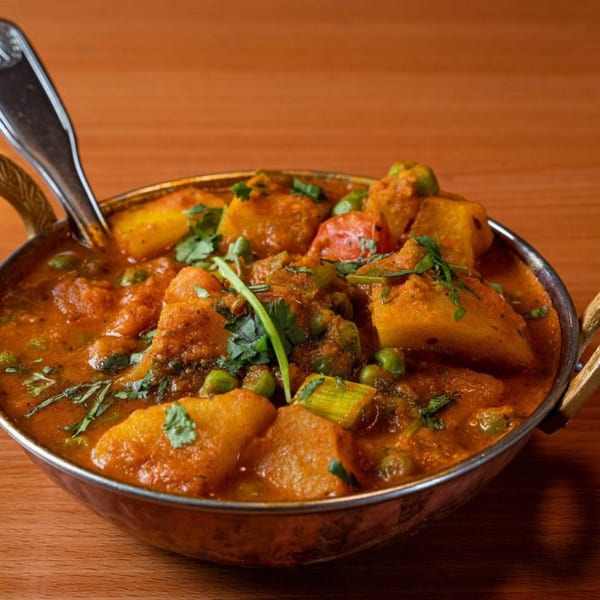 Aloo Matar, a Tibetan potato and pea curry, in a bronze bowl with a spoon.