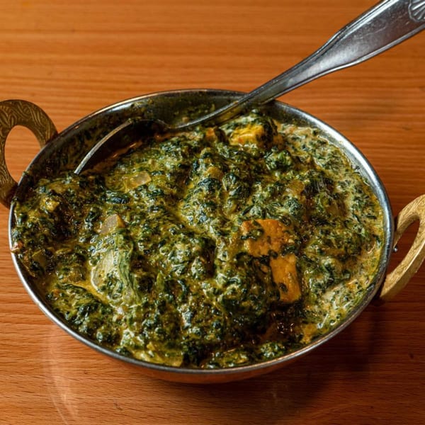 A metal bowl of creamy green spinach curry with paneer, served on a wooden table.