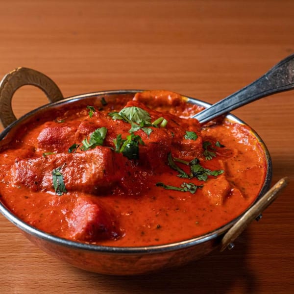 Yak and Yeti's vibrant red curry with chicken pieces, garnished with fresh cilantro in a metal bowl.