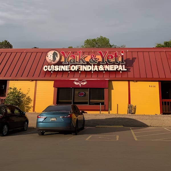The exterior of Yak & Yeti restaurant, with a red roof, yellow walls, and two cars parked outside.