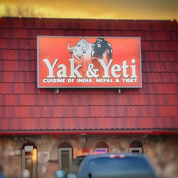 Yak & Yeti restaurant sign with a yak and yeti graphic, on a red-tiled roof.