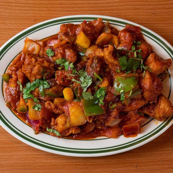 Spicy Tibetan chili chicken with bell peppers, onions, and cilantro on a white plate with green stripes.