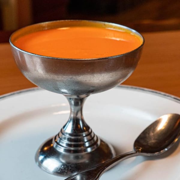 A silver goblet filled with orange soup sits on a white plate with a spoon.