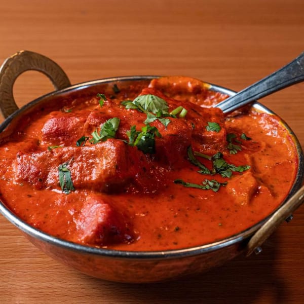 Yak and Yeti's vibrant red curry with chicken and fresh cilantro in a metal bowl.